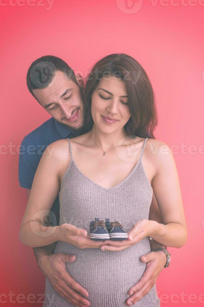 young pregnant couple holding newborn baby shoes photo