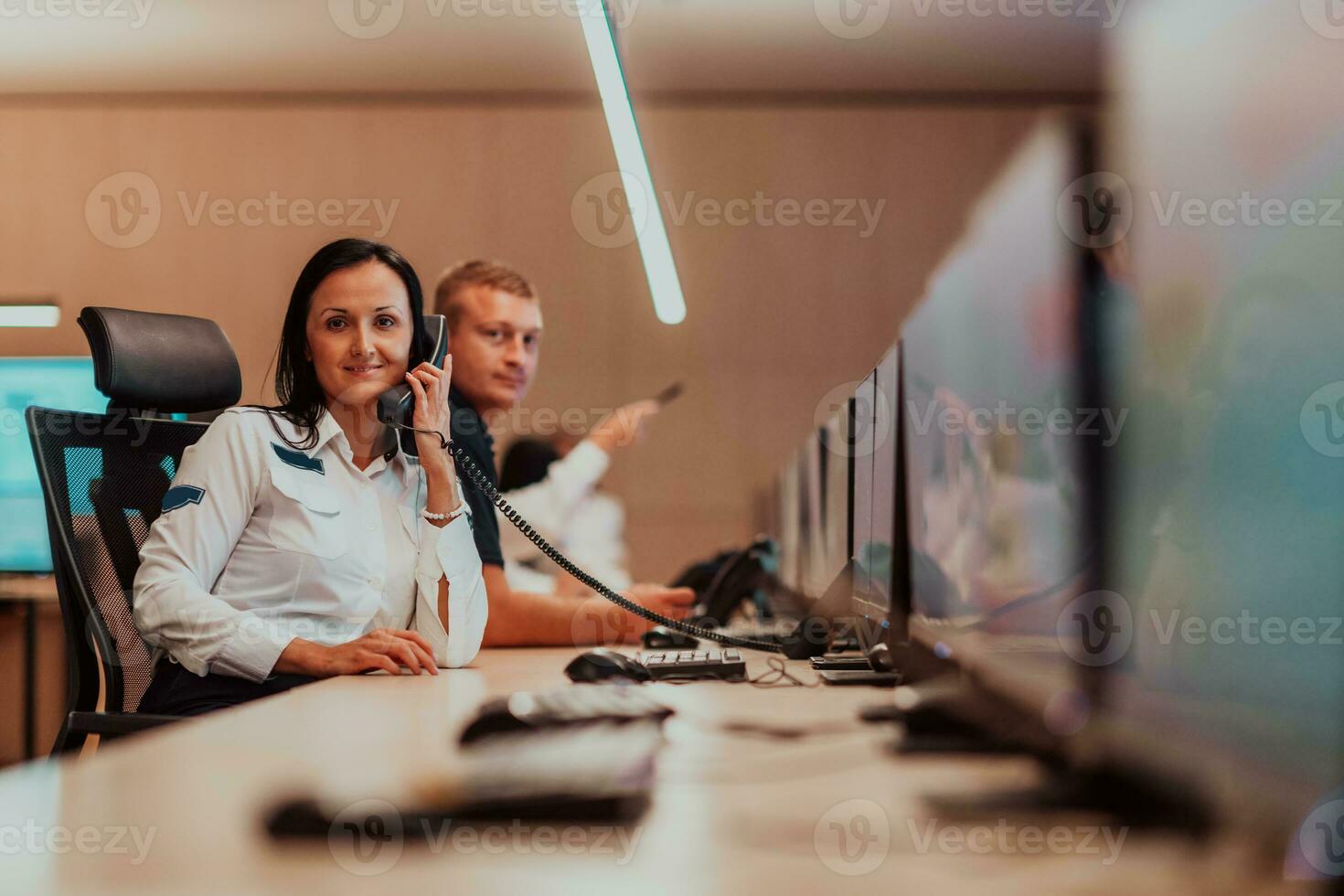 Female security guard operator talking on the phone while working at workstation with multiple displays Security guards working on multiple monitors photo