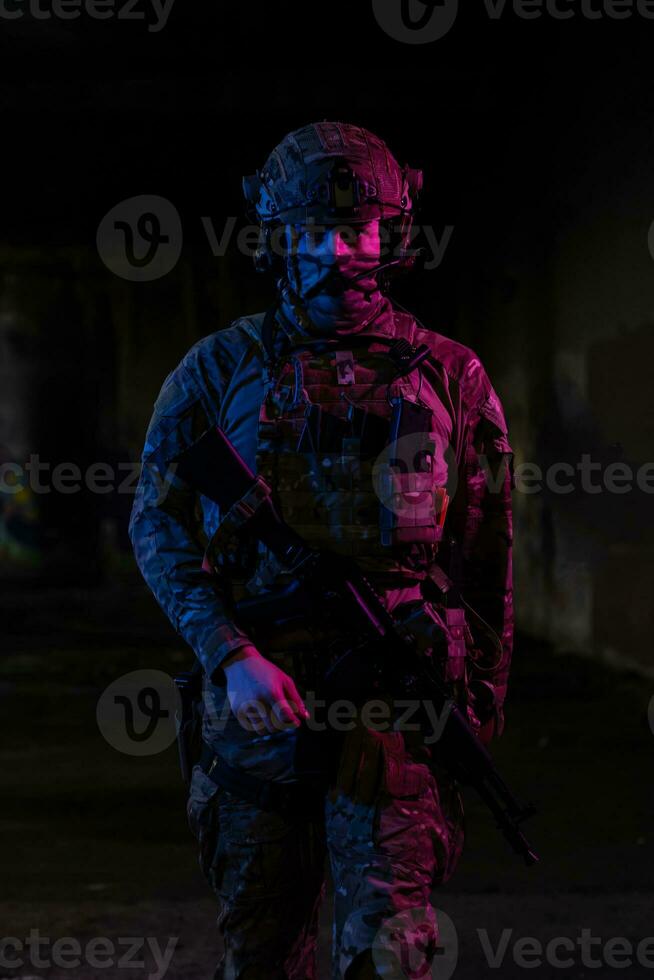 Army soldier in Combat Uniforms with an assault rifle and combat helmet night mission dark background. Blue and purple gel light effect. photo
