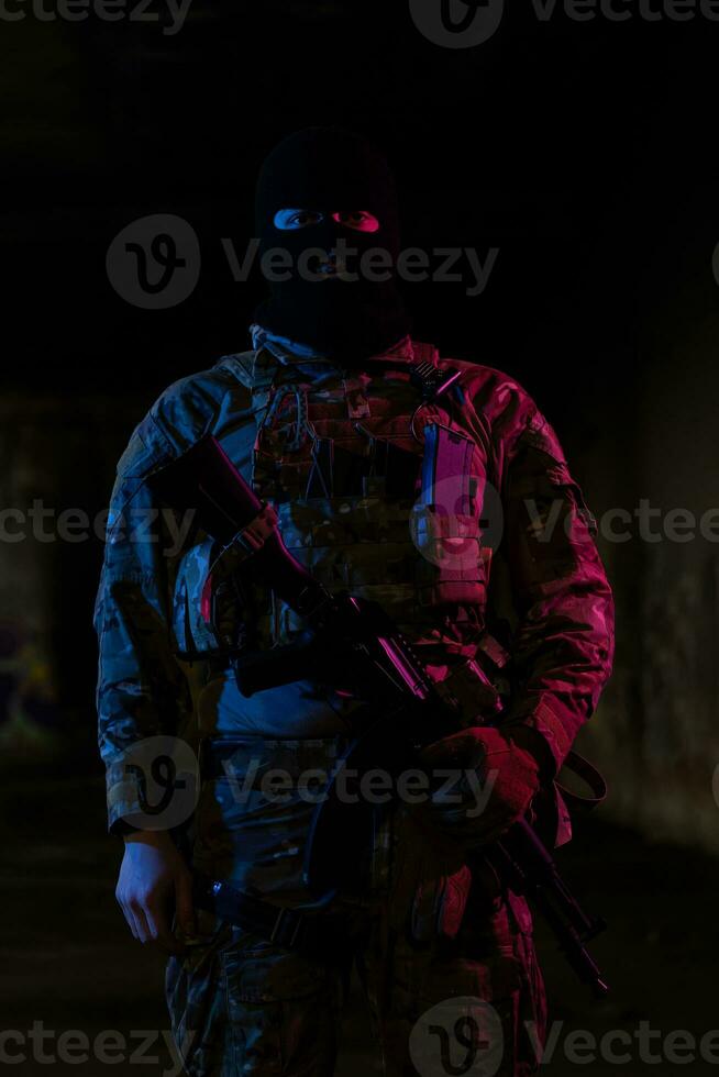 Army soldier in Combat Uniforms with an assault rifle and combat helmet night mission dark background. Blue and purple gel light effect. photo