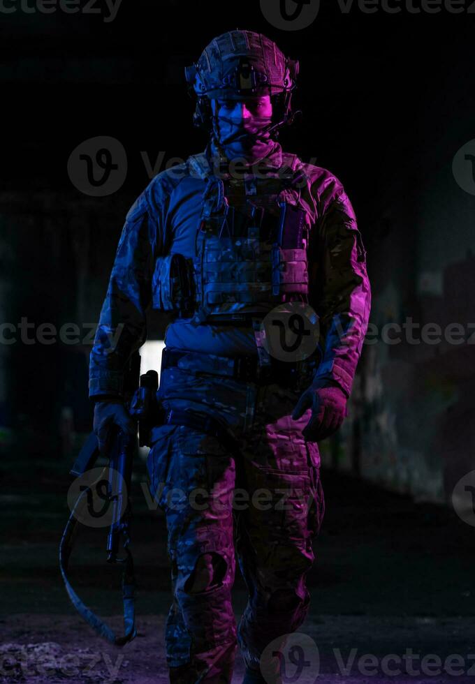 Army soldier in Combat Uniforms with an assault rifle and combat helmet night mission dark background. Blue and purple gel light effect. photo