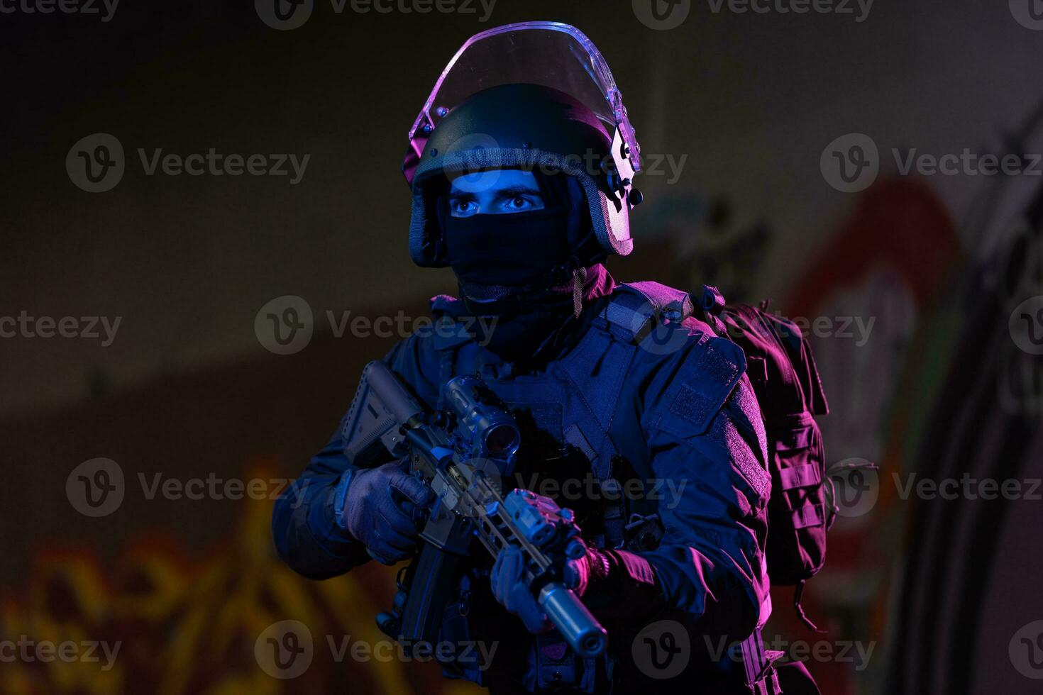 Army soldier in Combat Uniforms with an assault rifle and combat helmet night mission dark background. Blue and purple gel light effect. photo