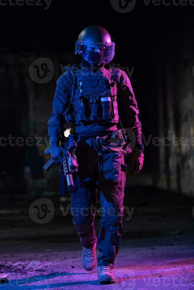 Army soldier in Combat Uniforms with an assault rifle and combat helmet night mission dark background. Blue and purple gel light effect. photo