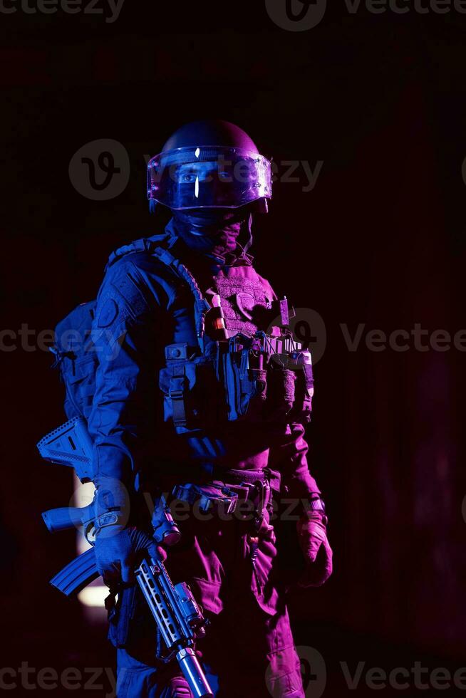 Army soldier in Combat Uniforms with an assault rifle and combat helmet night mission dark background. Blue and purple gel light effect. photo