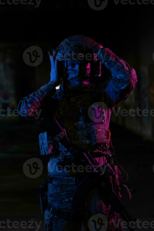 Ejército soldado en combate uniformes con un asalto rifle y combate casco noche misión oscuro antecedentes. azul y púrpura gel ligero efecto. foto