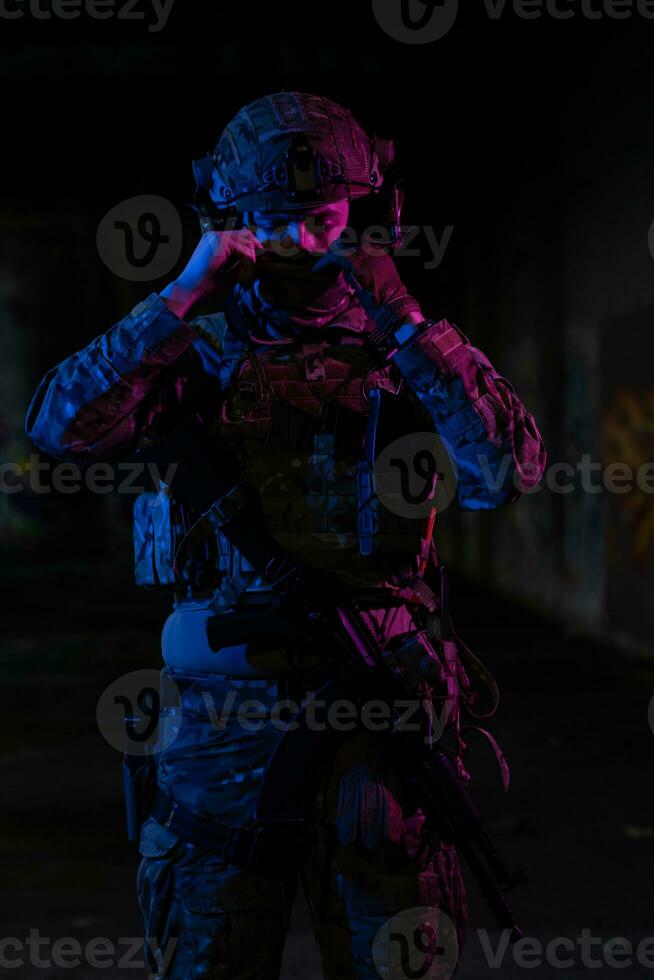 Ejército soldado en combate uniformes con un asalto rifle y combate casco noche misión oscuro antecedentes. azul y púrpura gel ligero efecto. foto