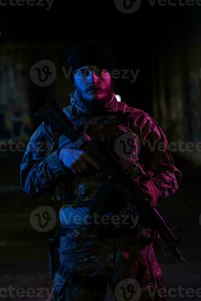Army soldier in Combat Uniforms with an assault rifle and combat helmet night mission dark background. Blue and purple gel light effect. photo