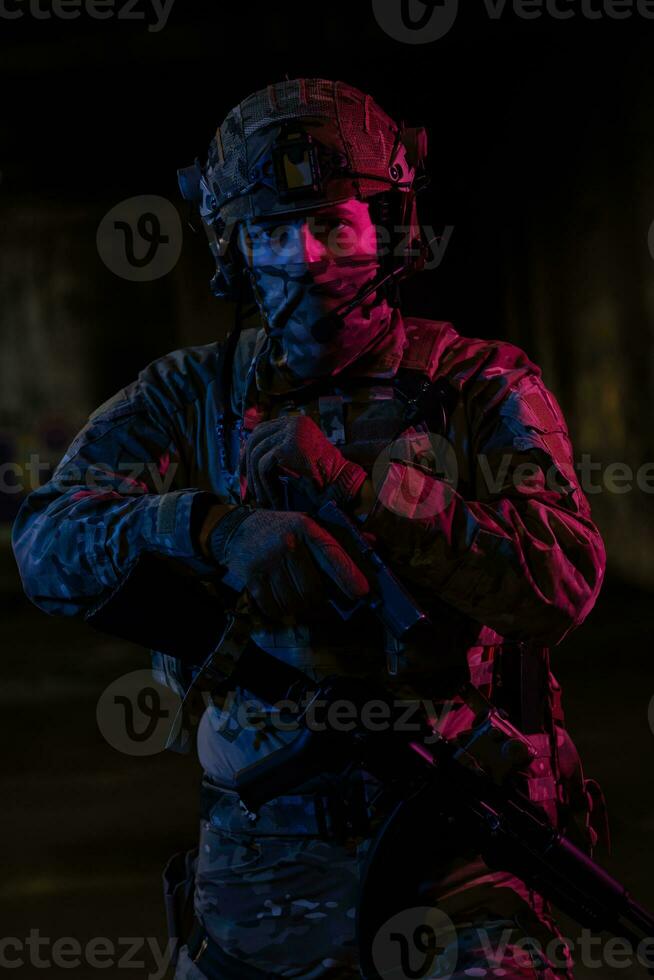 Army soldier in Combat Uniforms with an assault rifle and combat helmet night mission dark background. Blue and purple gel light effect. photo