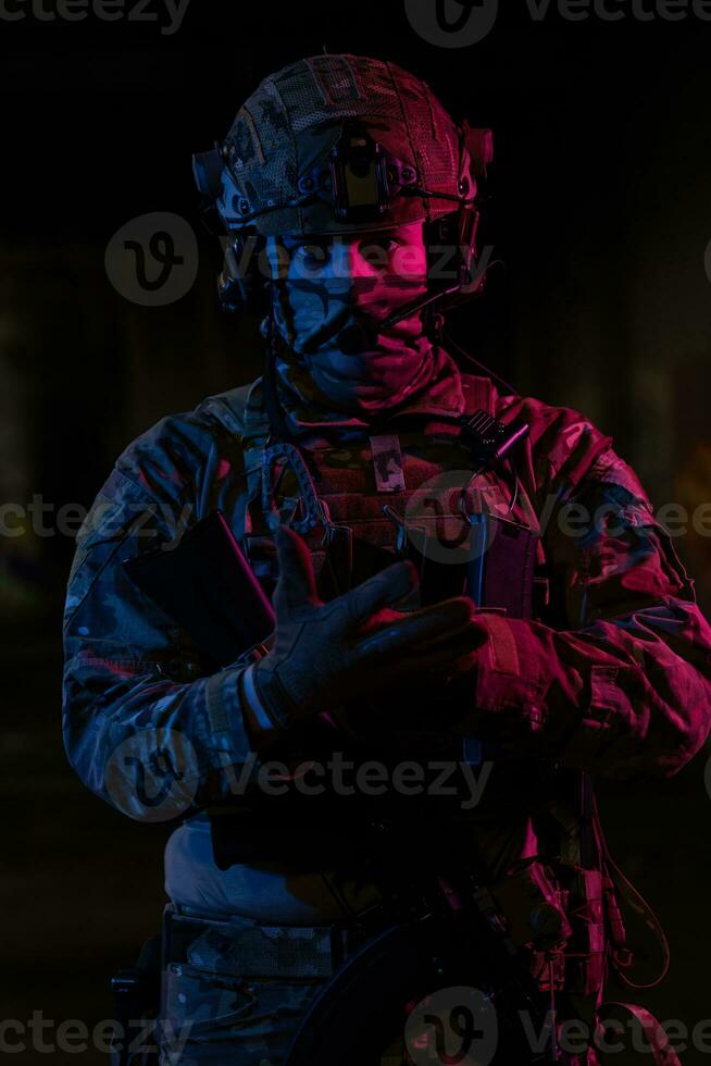 foto de un completamente equipado soldado en negro armadura táctico chaleco y guantes en pie en negro antecedentes de cerca frente vista.