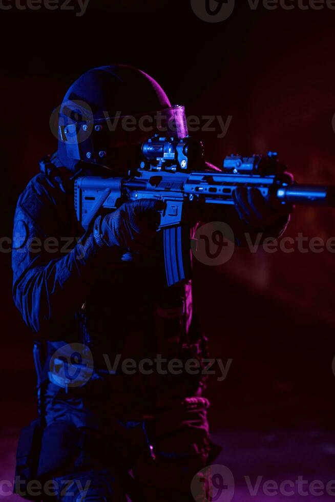 Army soldier in Combat Uniforms with an assault rifle and combat helmet night mission dark background. Blue and purple gel light effect. photo