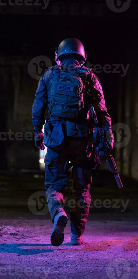 Army soldier in Combat Uniforms with an assault rifle and combat helmet night mission dark background. Blue and purple gel light effect. photo