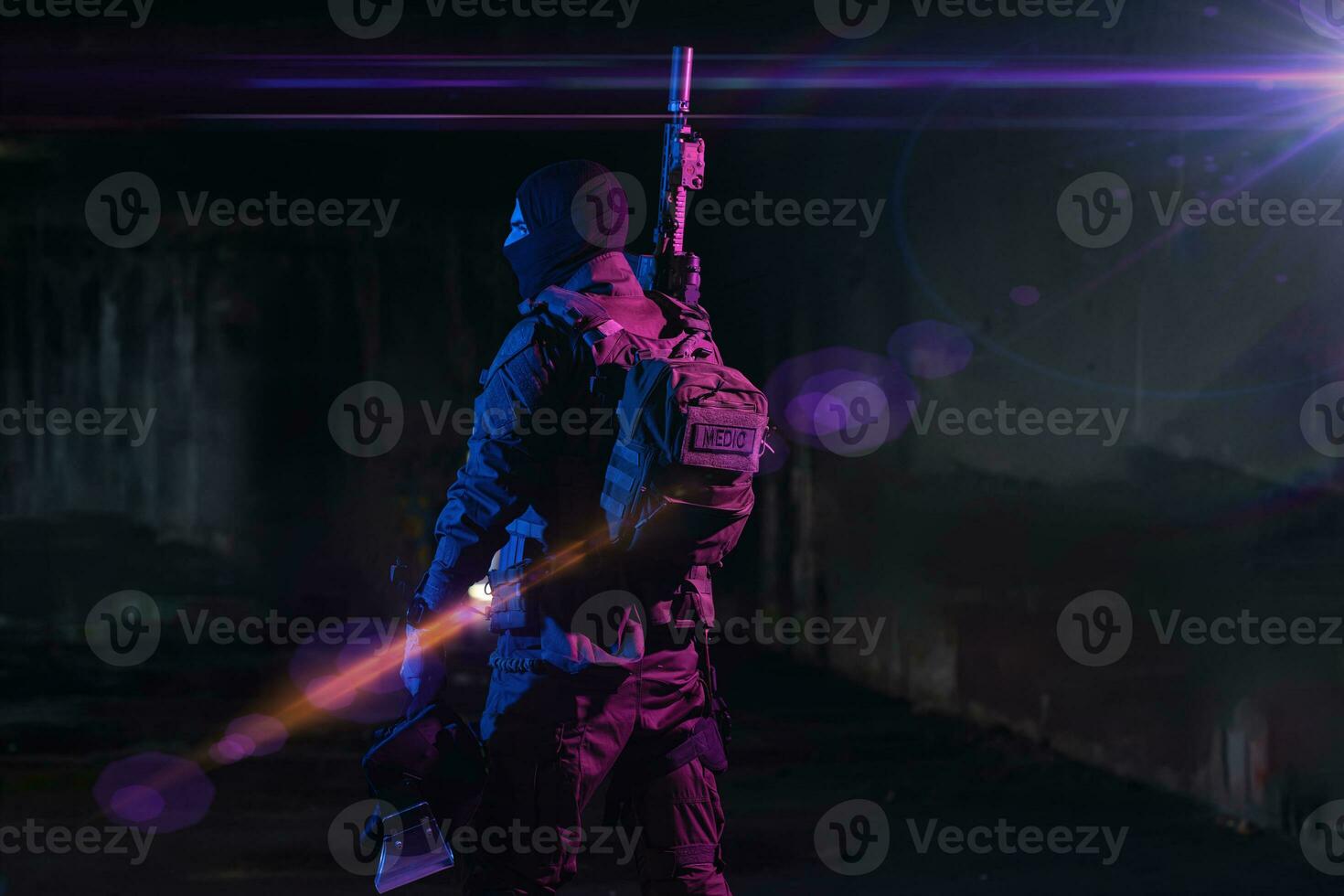 Army soldier in Combat Uniforms with an assault rifle and combat helmet night mission dark background. Blue and purple gel light effect. photo