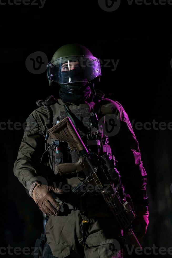 Army soldier in Combat Uniforms with an assault rifle and combat helmet night mission dark background. Blue and purple gel light effect. photo