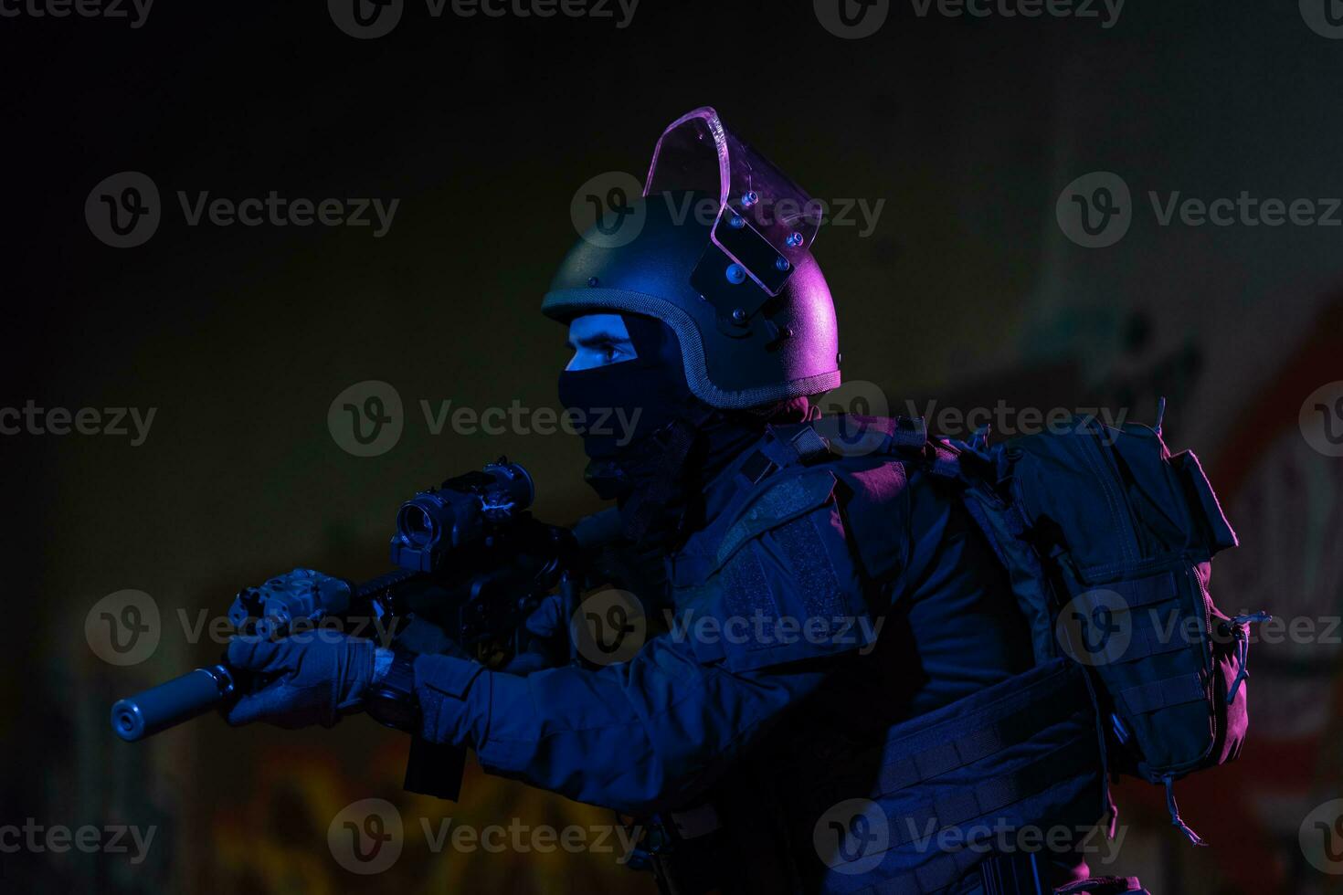 Army soldier in Combat Uniforms with an assault rifle and combat helmet night mission dark background. Blue and purple gel light effect. photo