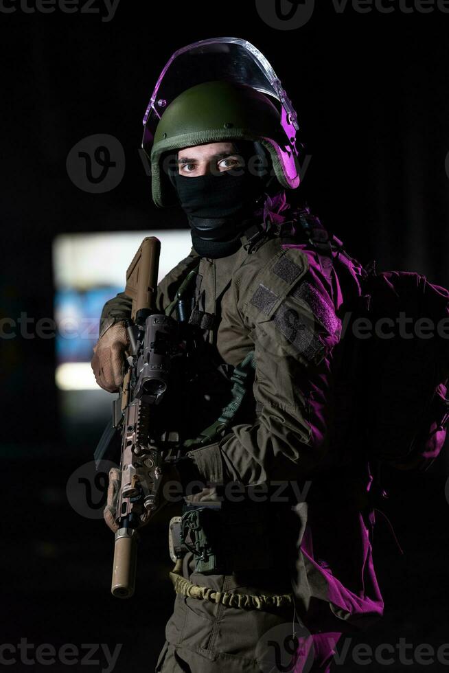 Ejército soldado en combate uniformes con un asalto rifle y combate casco noche misión oscuro antecedentes. azul y púrpura gel ligero efecto. foto