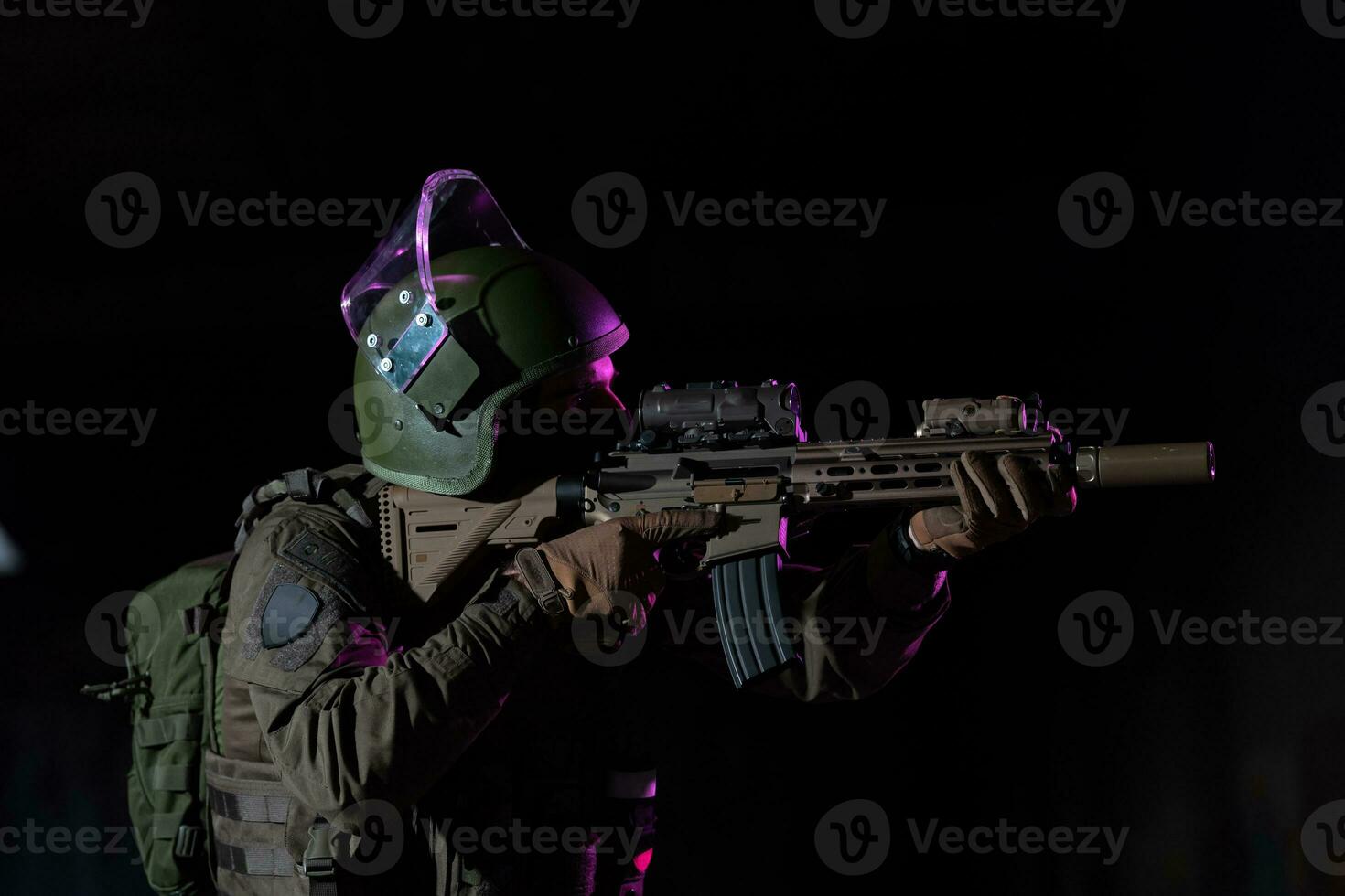 Army soldier in Combat Uniforms with an assault rifle and combat helmet night mission dark background. Blue and purple gel light effect. photo