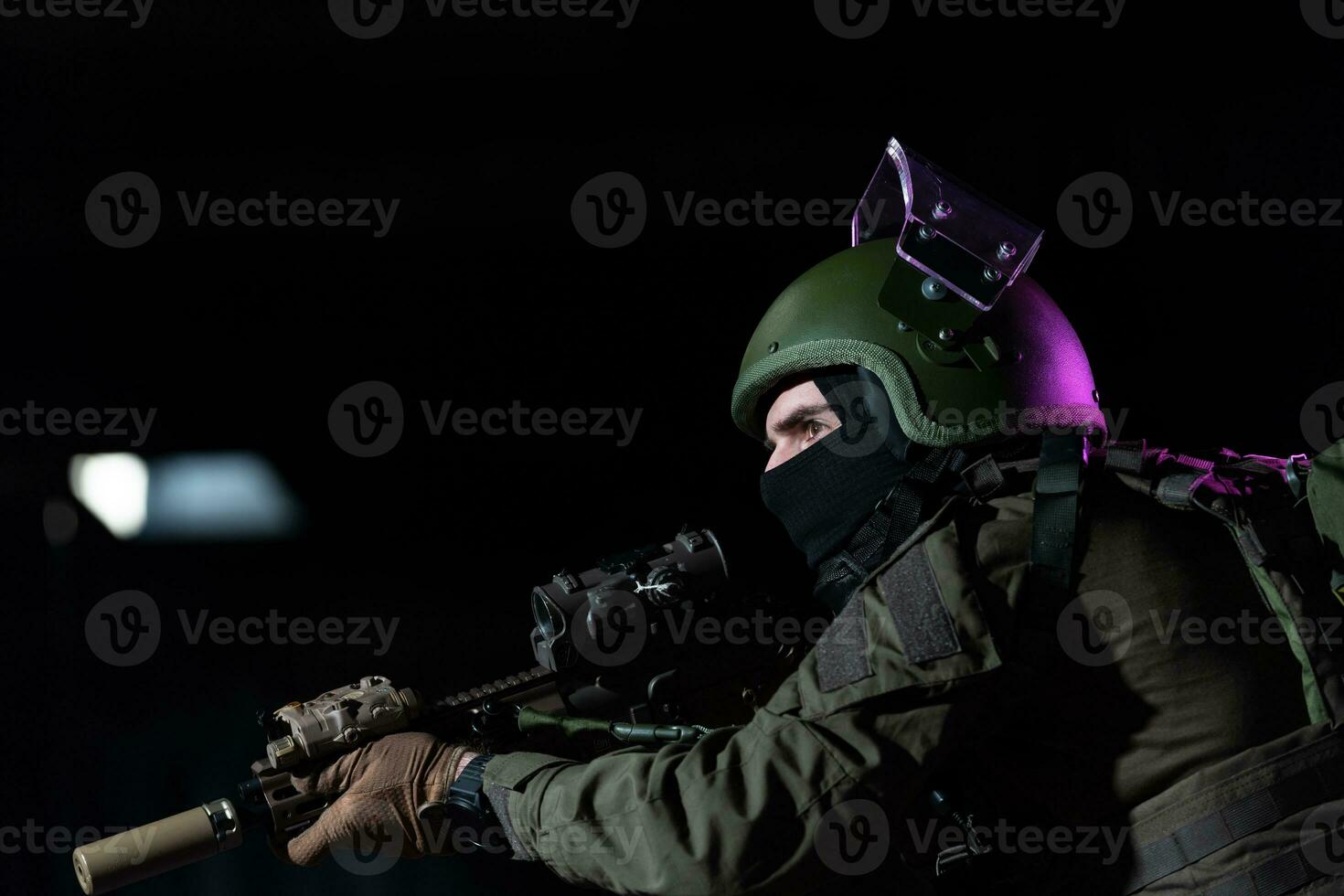 Army soldier in Combat Uniforms with an assault rifle and combat helmet night mission dark background. Blue and purple gel light effect. photo