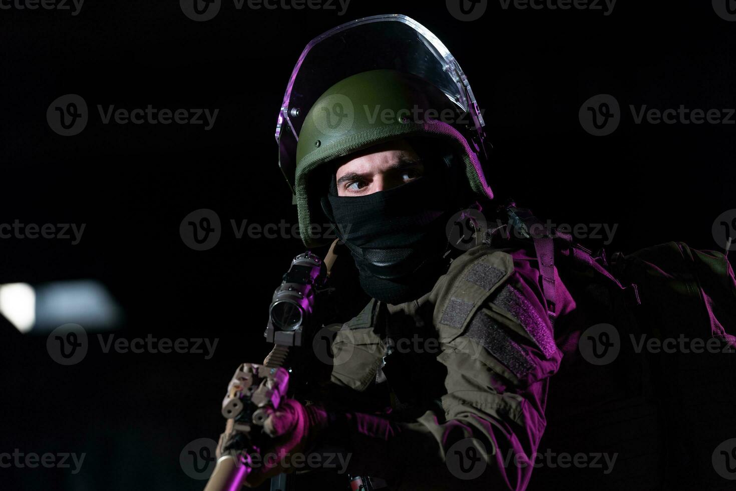 Army soldier in Combat Uniforms with an assault rifle and combat helmet night mission dark background. Blue and purple gel light effect. photo