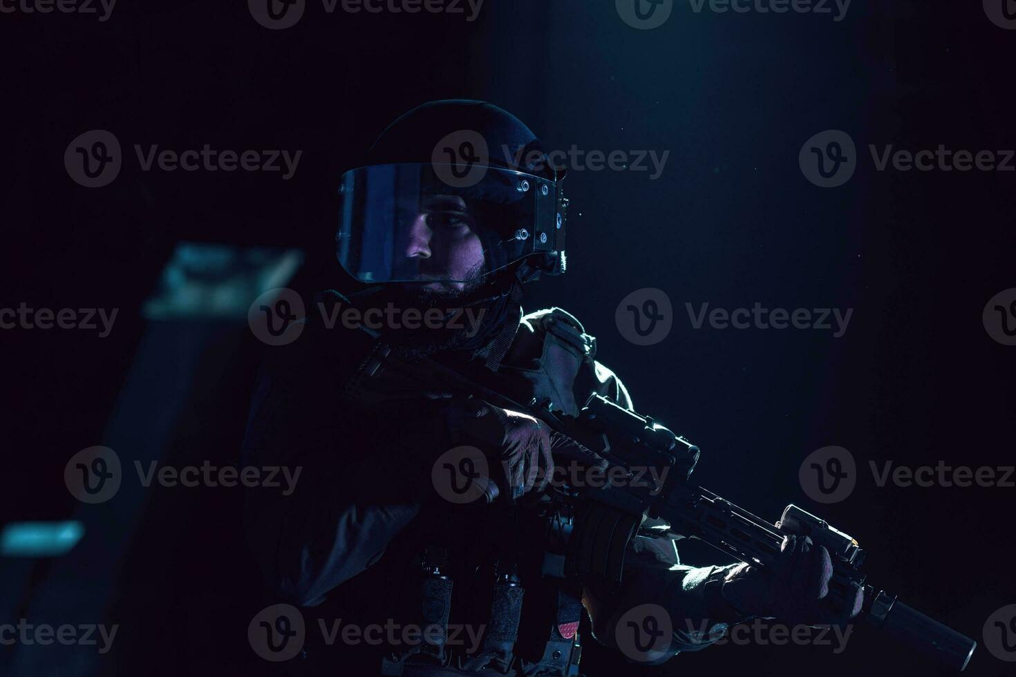 Army soldier in Combat Uniforms with an assault rifle and combat helmet night mission dark background. Blue and purple gel light effect. photo