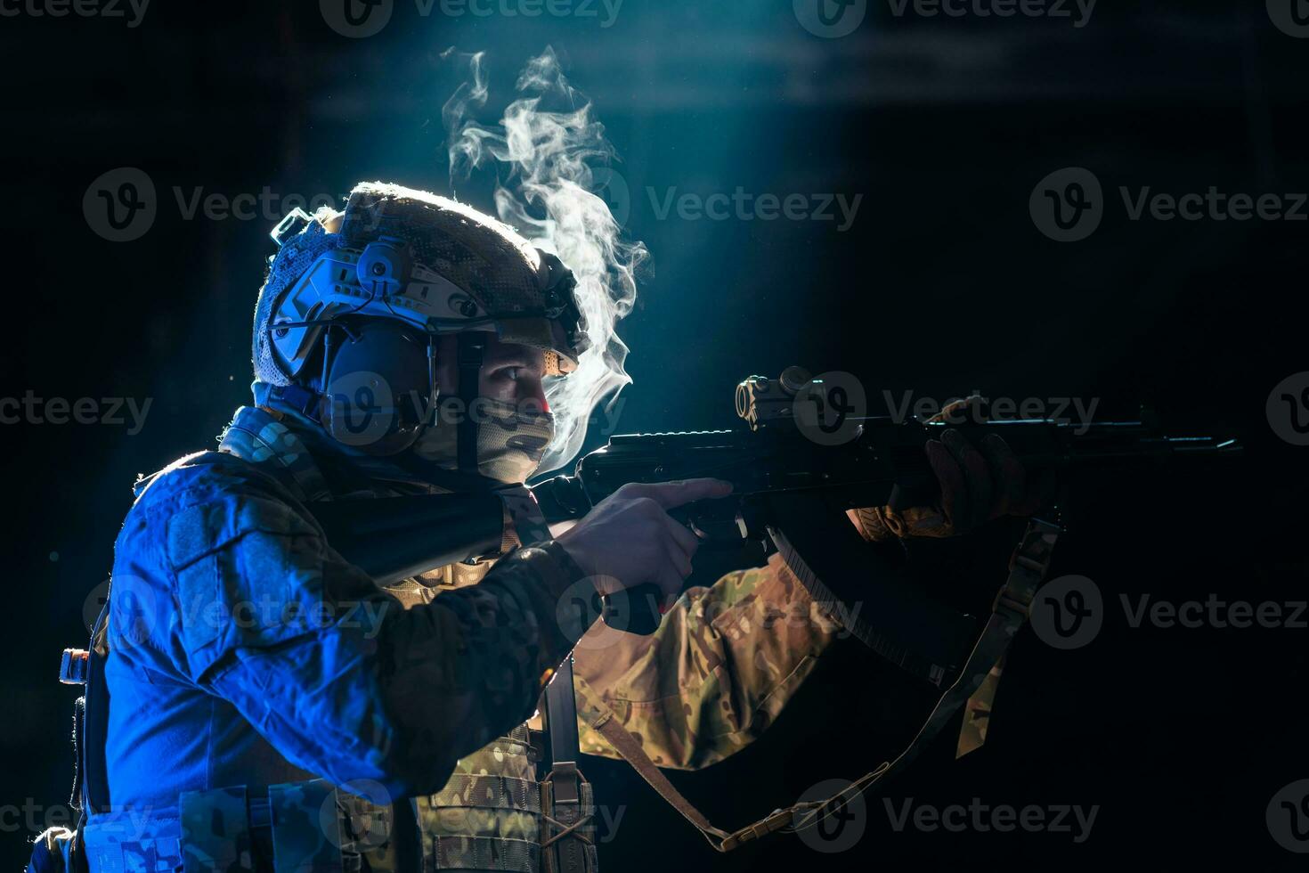 Army soldier in Combat Uniforms with an assault rifle and combat helmet night mission dark background. Blue and purple gel light effect. photo
