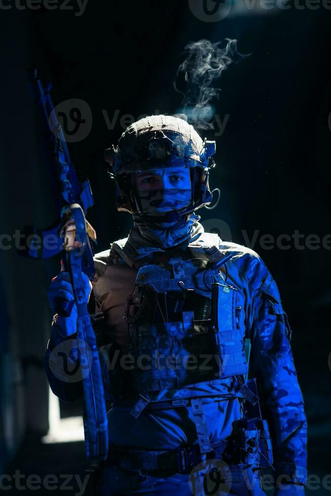 Army soldier in Combat Uniforms with an assault rifle and combat helmet night mission dark background. Blue and purple gel light effect. photo