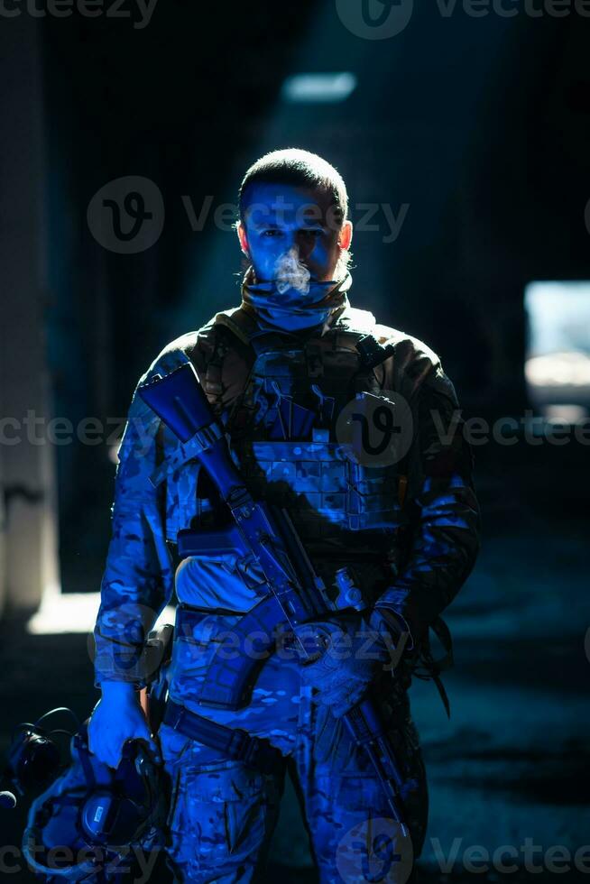 Army soldier in Combat Uniforms with an assault rifle and combat helmet night mission dark background. Blue and purple gel light effect. photo