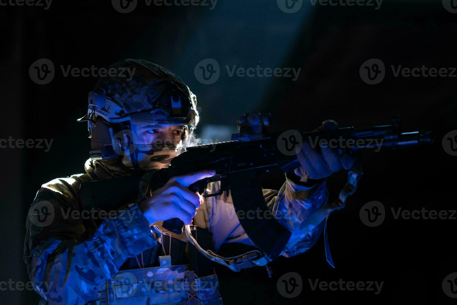 Army soldier in Combat Uniforms with an assault rifle and combat helmet night mission dark background. Blue and purple gel light effect. photo