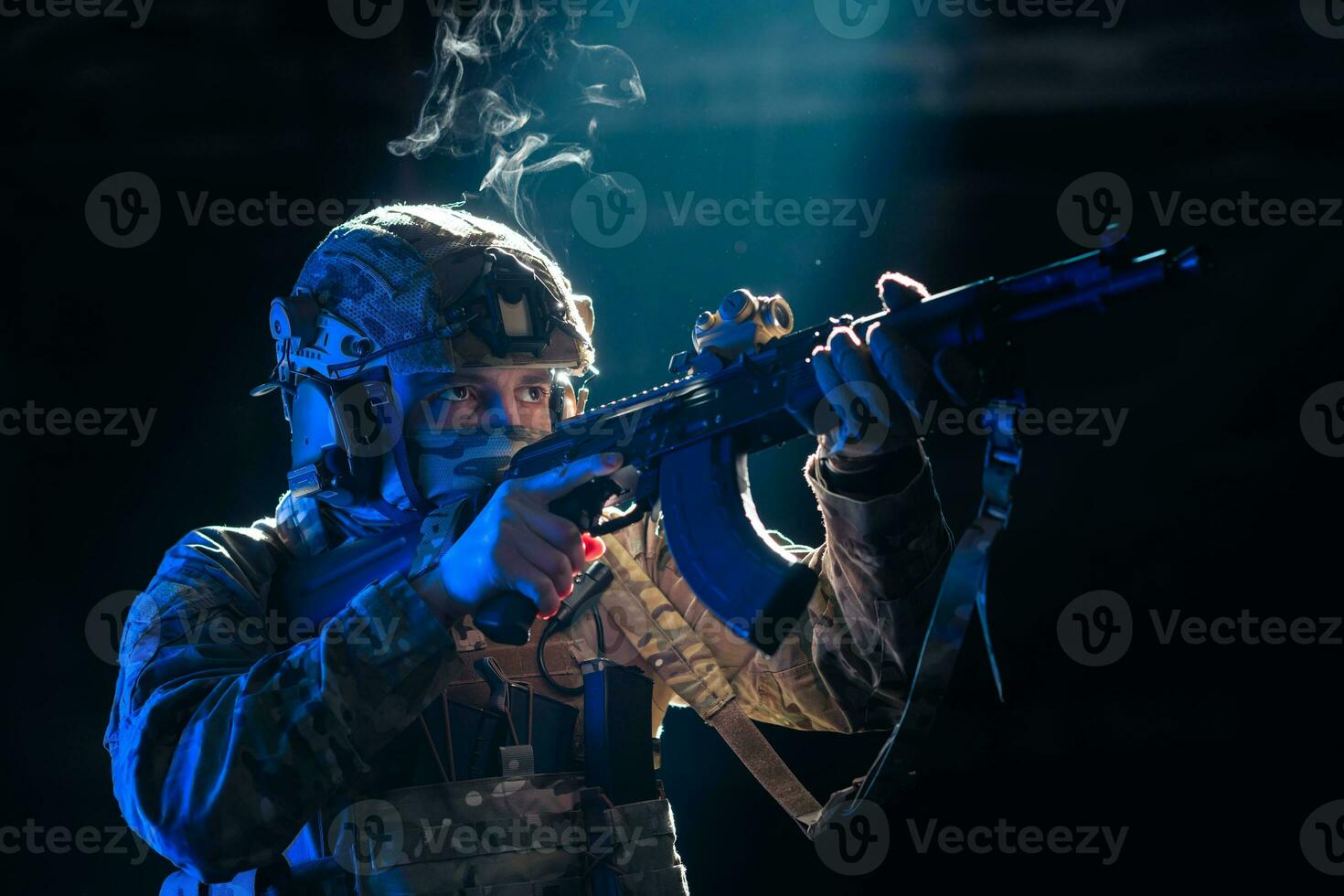 Army soldier in Combat Uniforms with an assault rifle and combat helmet night mission dark background. Blue and purple gel light effect. photo