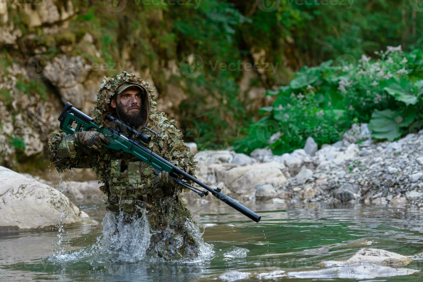A military man or airsoft player in a camouflage suit sneaking the river and aims from a sniper rifle to the side or to target. photo
