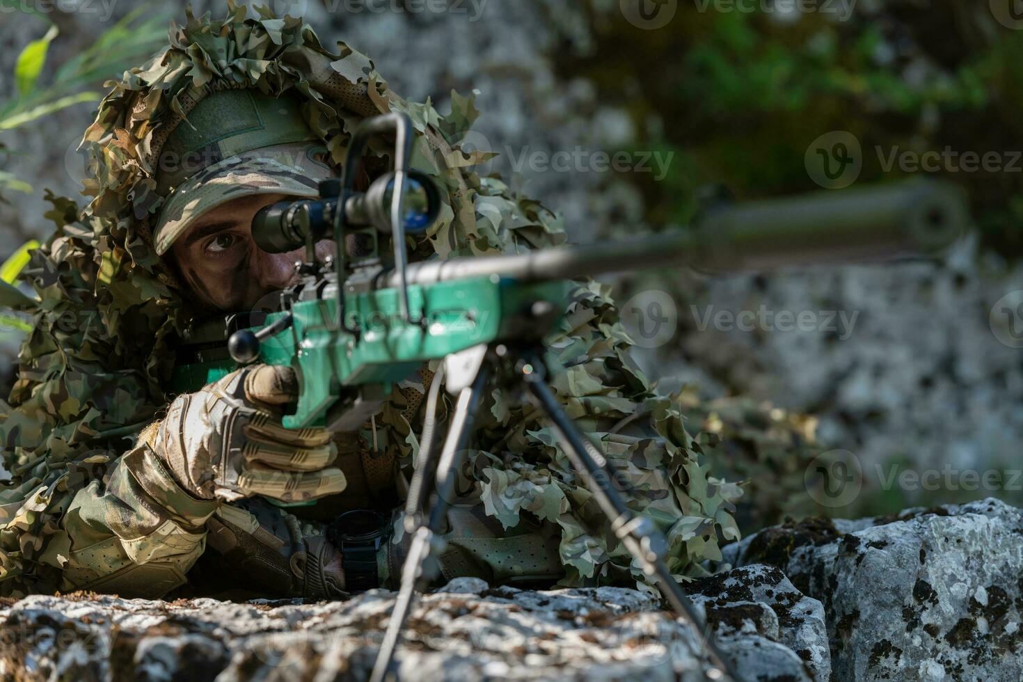 A military man or airsoft player in a camouflage suit sneaking the river and aims from a sniper rifle to the side or to target. photo