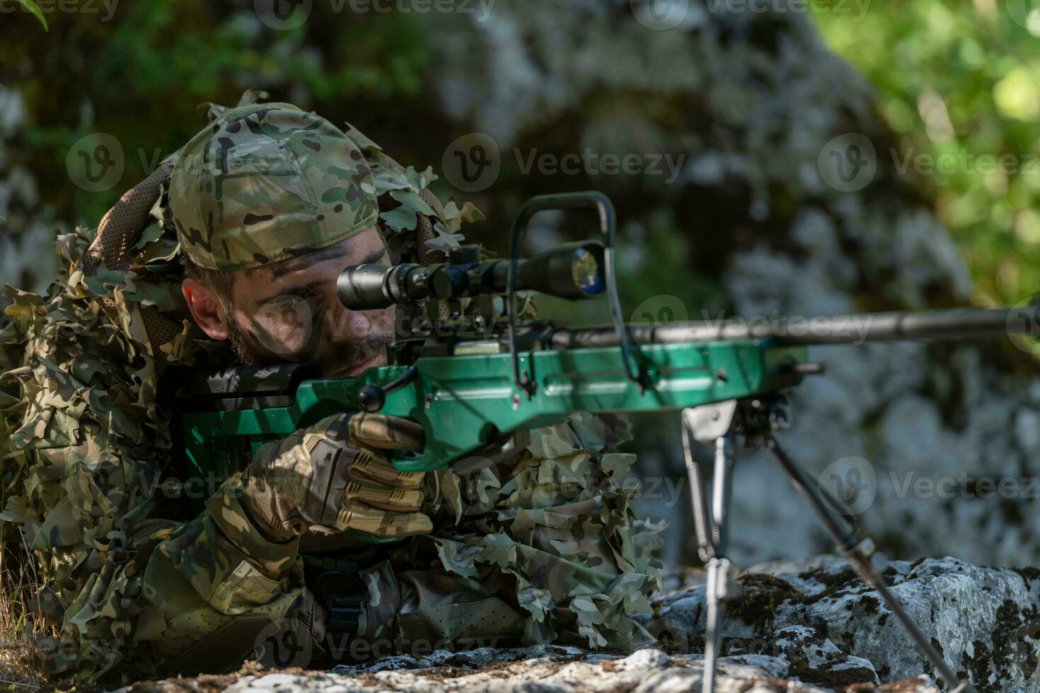 A military man or airsoft player in a camouflage suit sneaking the river and aims from a sniper rifle to the side or to target. photo