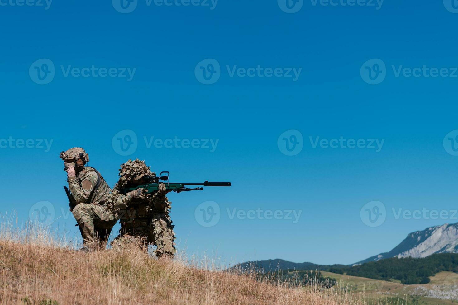 A sniper team squad of soldiers is going undercover. Sniper assistant and team leader walking and aiming in nature with yellow grass and blue sky. Tactical camouflage uniform. photo