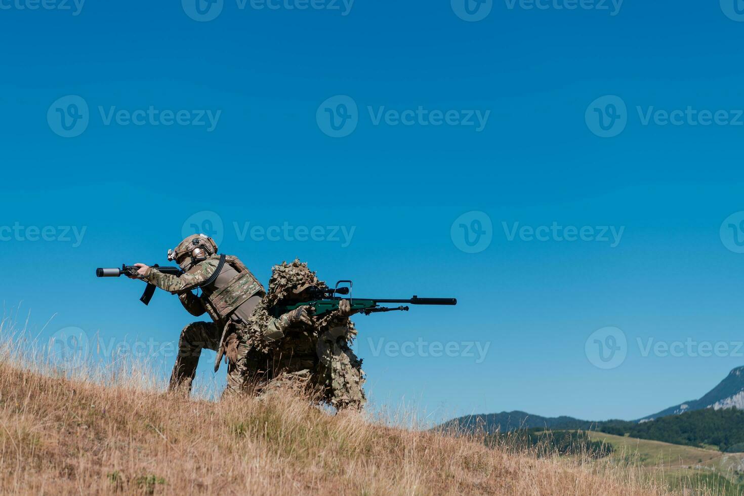 A sniper team squad of soldiers is going undercover. Sniper assistant and team leader walking and aiming in nature with yellow grass and blue sky. Tactical camouflage uniform. photo