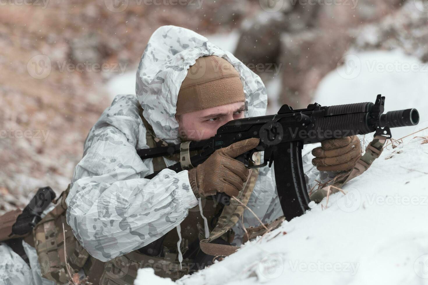 Winter war in the Arctic mountains. Operation in cold conditions.Soldier in winter camouflaged uniform in Modern warfare army on a snow day on forest battlefield with a rifle. Selective focus photo