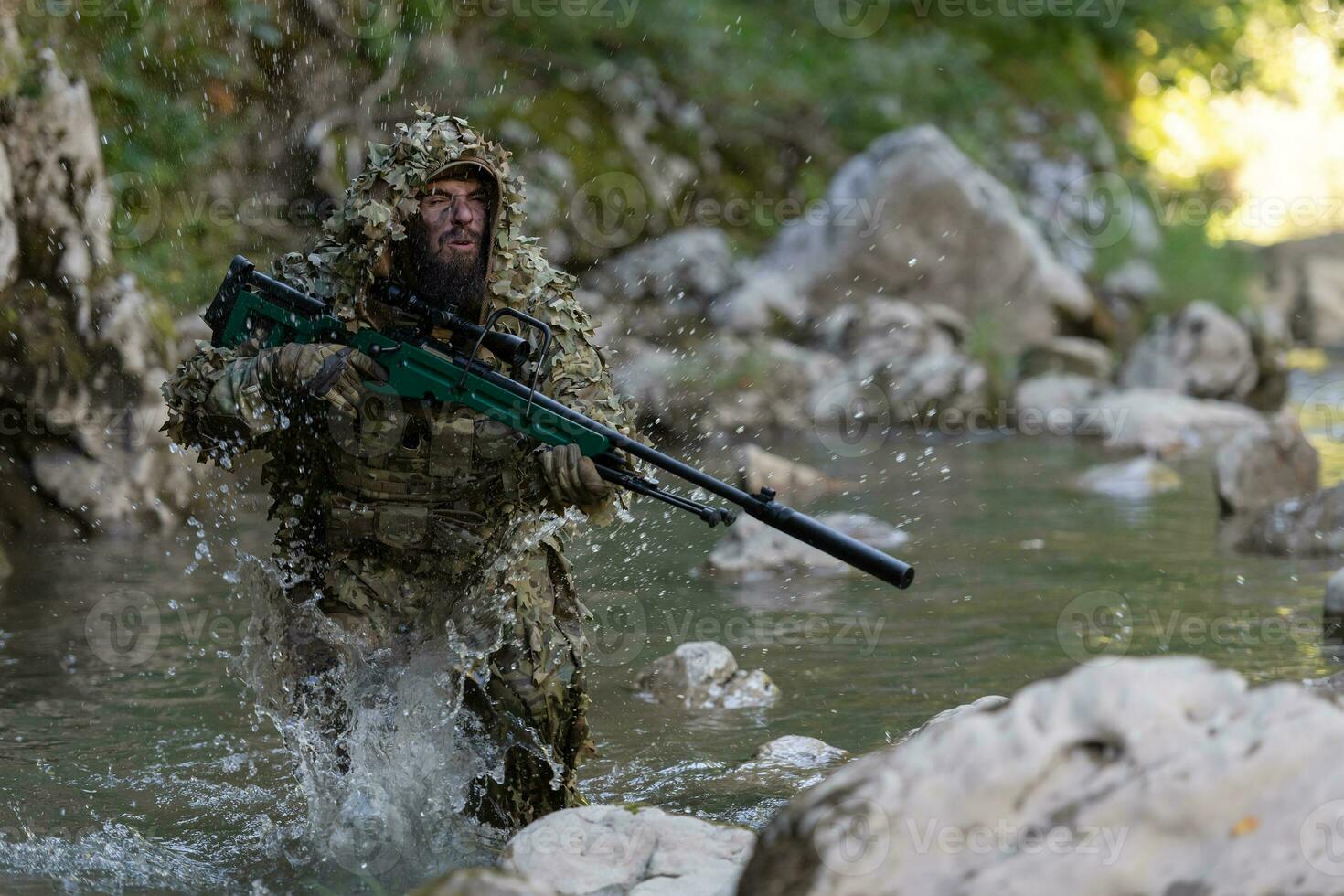 A military man or airsoft player in a camouflage suit sneaking the river and aims from a sniper rifle to the side or to target. photo