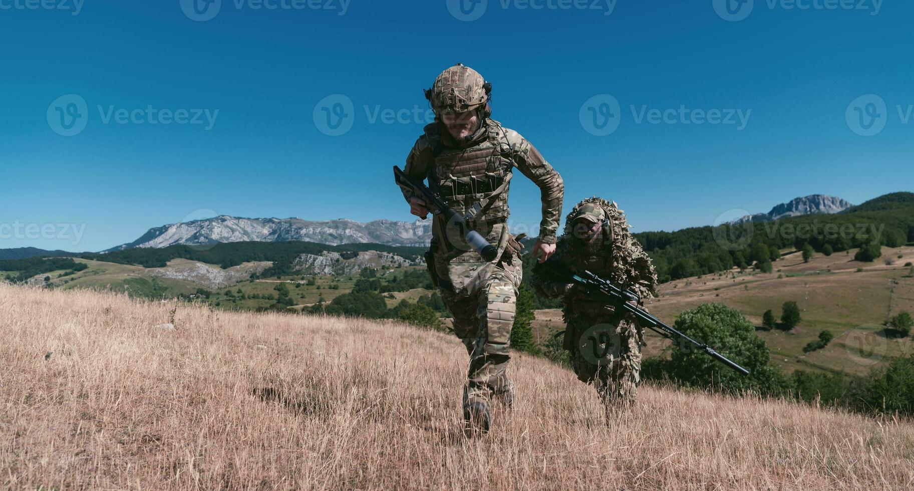 A sniper team squad of soldiers is going undercover. Sniper assistant and team leader walking and aiming in nature with yellow grass and blue sky. Tactical camouflage uniform. photo