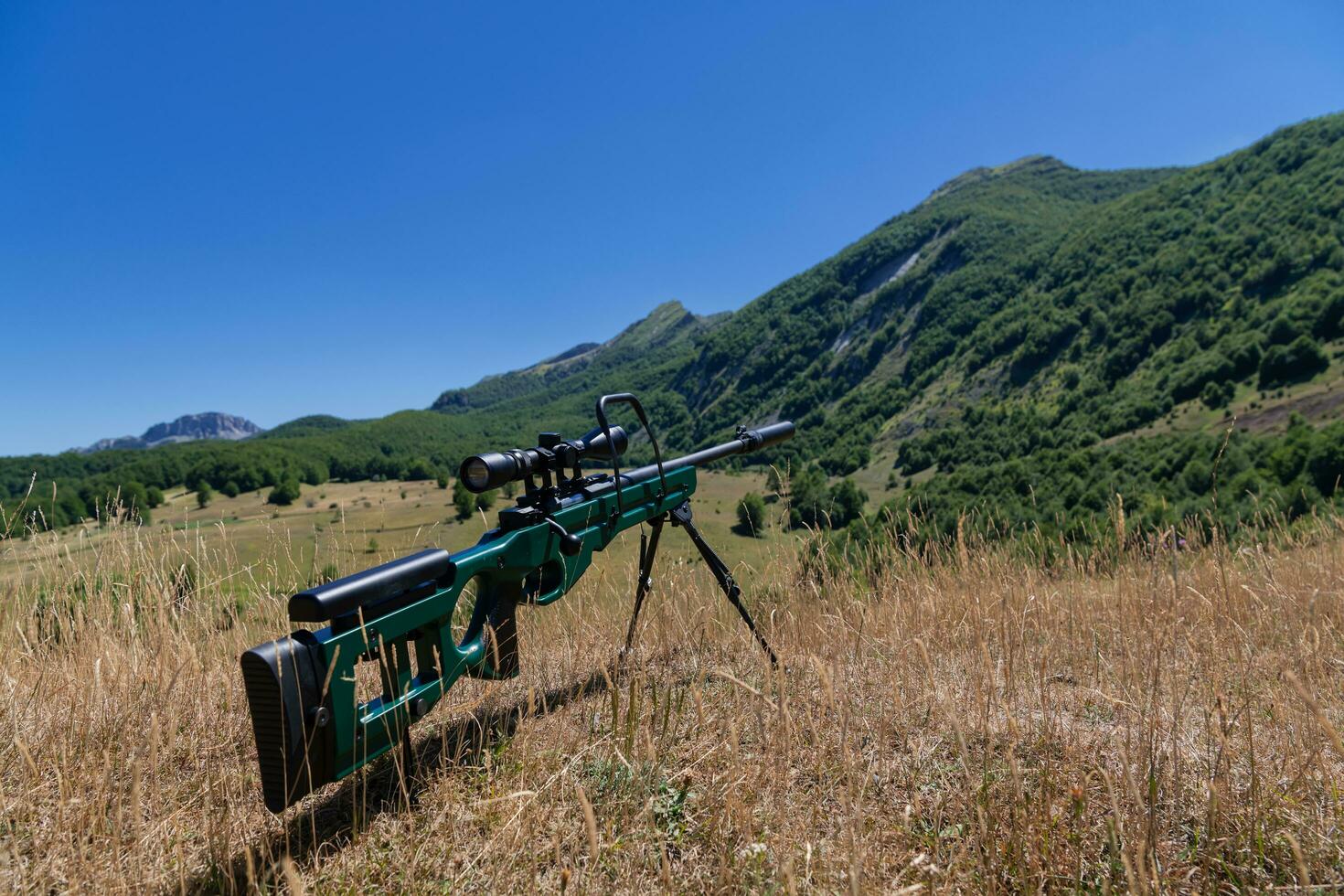 A green military sniper rifle with a scope for long distance tactical modern warfare in yellow grass blue sky photo