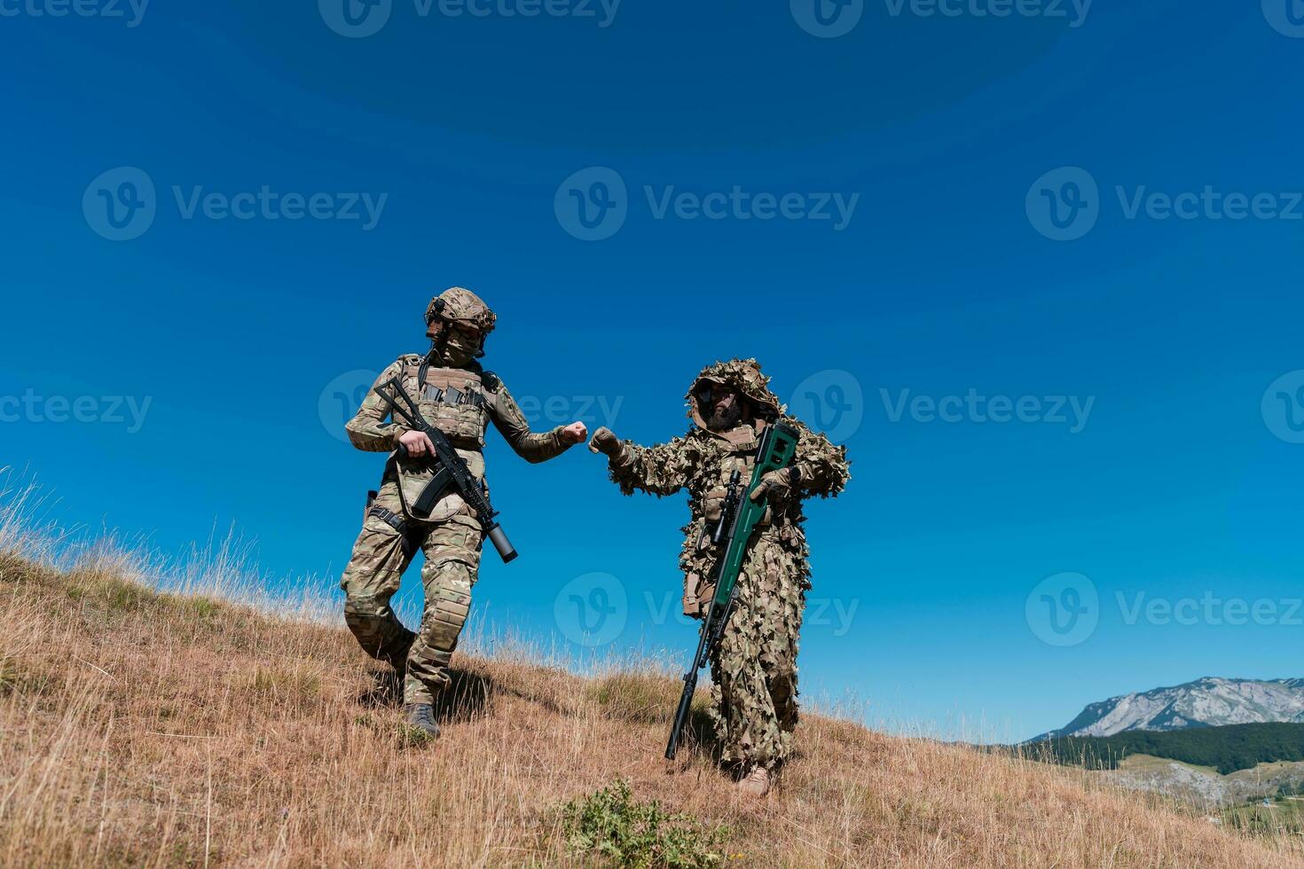 A sniper team squad of soldiers is going undercover. Sniper assistant and team leader walking and aiming in nature with yellow grass and blue sky. Tactical camouflage uniform. photo