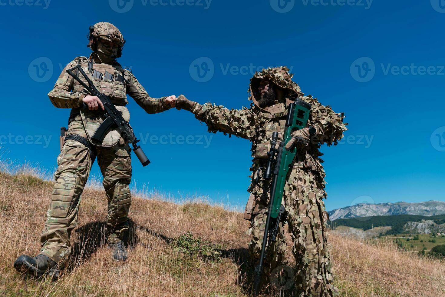 A sniper team squad of soldiers is going undercover. Sniper assistant and team leader walking and aiming in nature with yellow grass and blue sky. Tactical camouflage uniform. photo