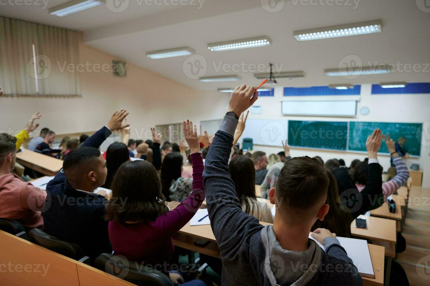 Raised hands and arms of large group of people in class room photo