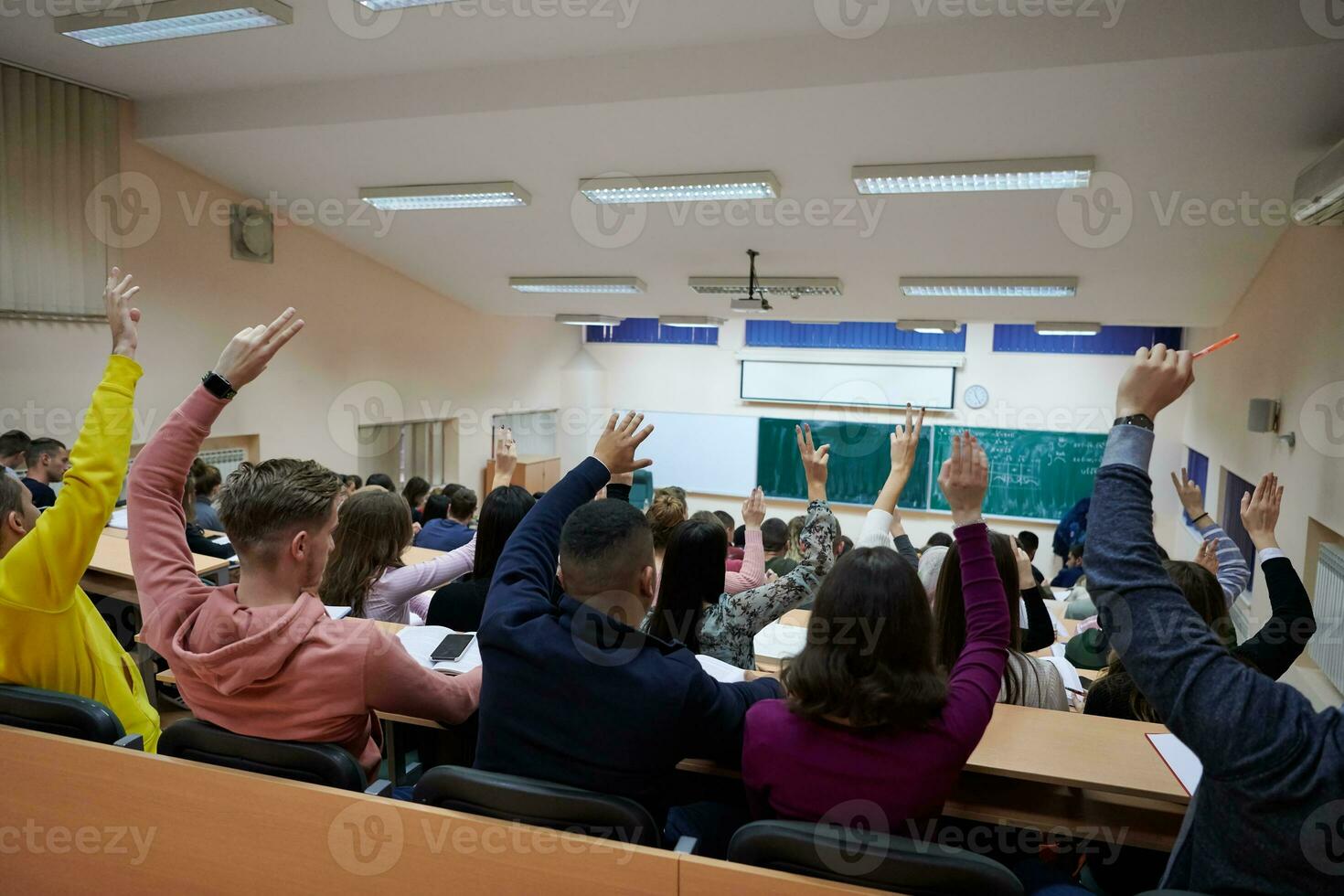 Raised hands and arms of large group of people in class room photo