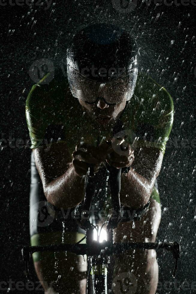 atleta de triatlón montando bicicleta rápido en una noche lluviosa foto