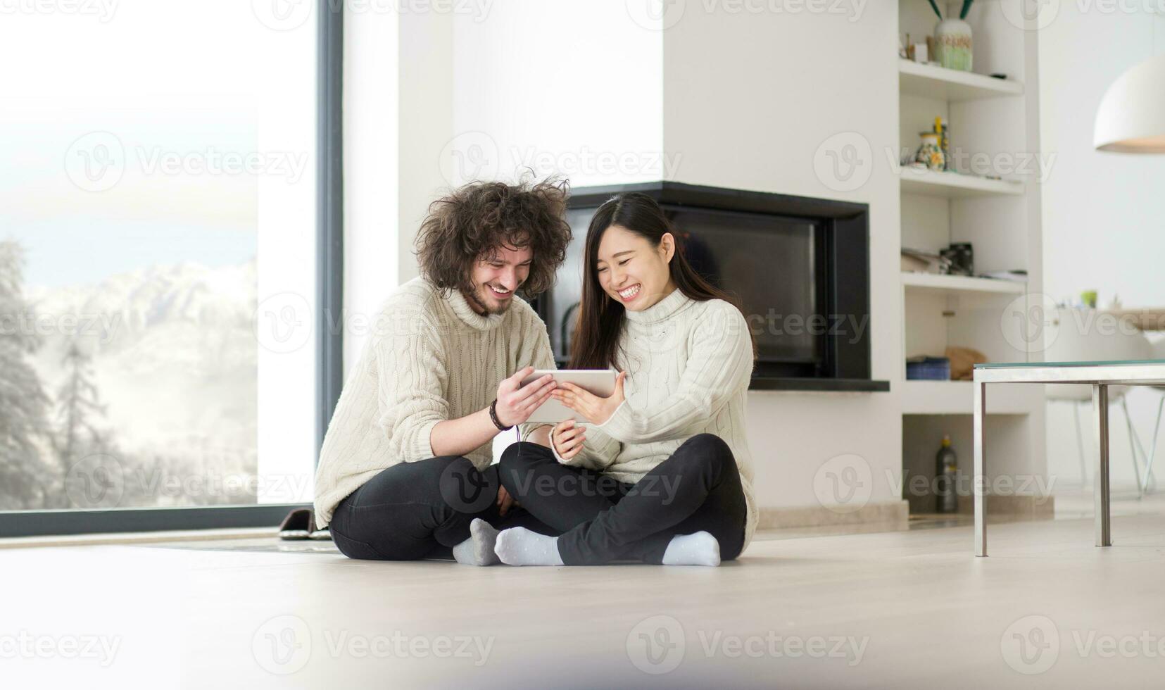 multiethnic couple using tablet computer in front of fireplace photo