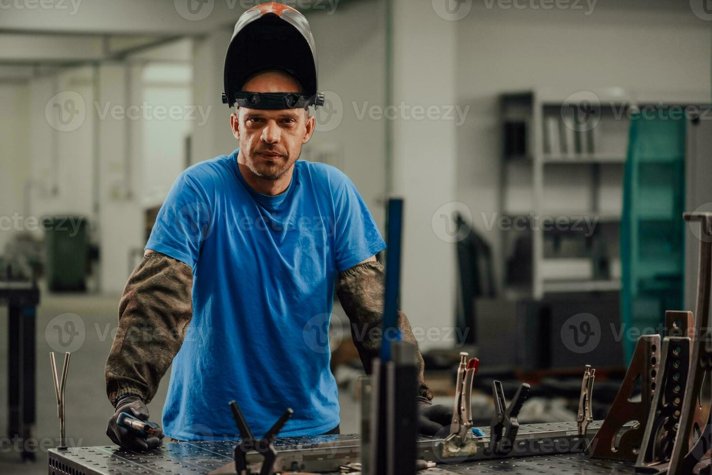 Portrait of Young Professional Heavy Industry Engineer. Worker Wearing Safety Vest and Hardhat Smiling on Camera. In the Background Unfocused Large Industrial Factory photo