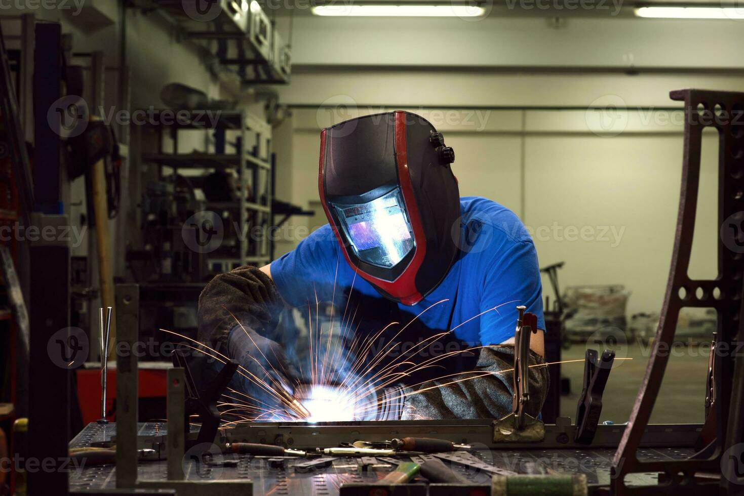 soldador profesional de la industria pesada que trabaja dentro de la fábrica, usa casco y comienza a soldar. enfoque selectivo foto