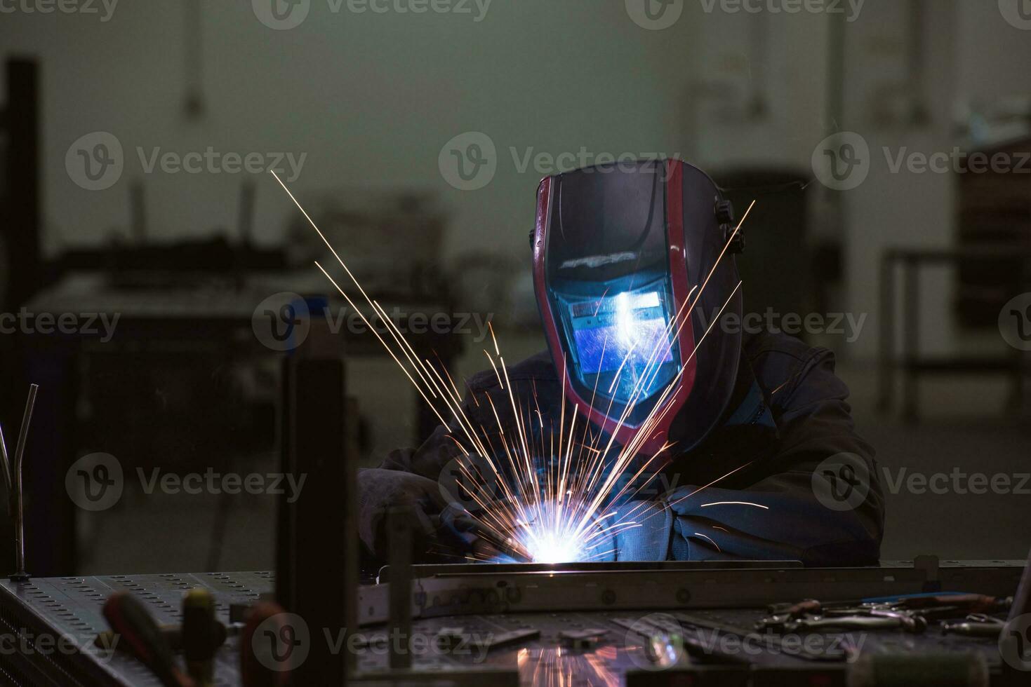 soldador profesional de la industria pesada que trabaja dentro de la fábrica, usa casco y comienza a soldar. enfoque selectivo foto