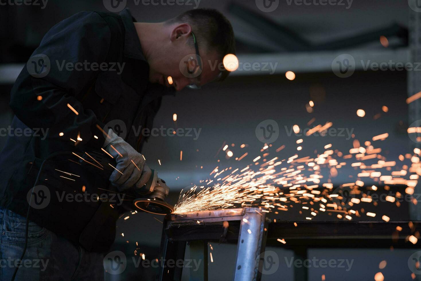 Heavy Industry Engineering Factory Interior with Industrial Worker Using Angle Grinder and Cutting a Metal Tube. Contractor in Safety Uniform and Hard Hat Manufacturing Metal Structures. photo