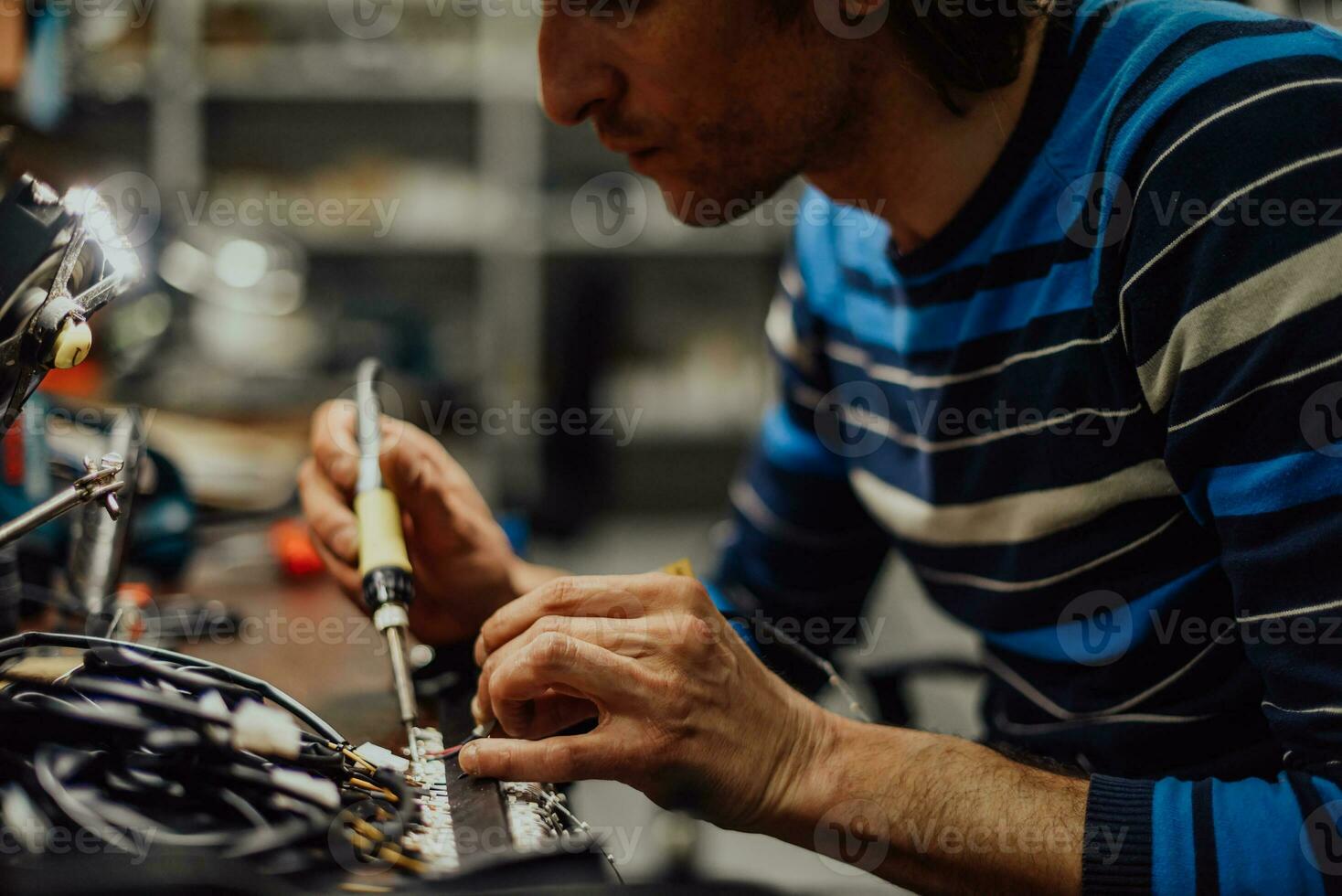 Industrial worker man soldering cables of manufacturing equipment in a factory. Selective focus photo