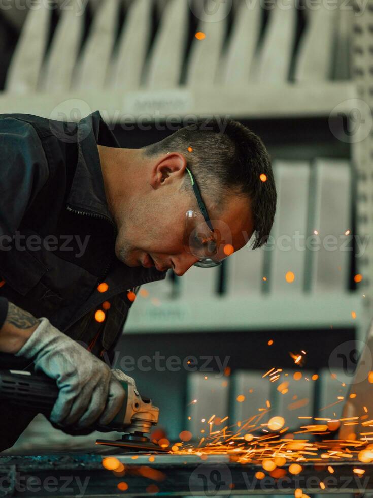 Heavy Industry Engineering Factory Interior with Industrial Worker Using Angle Grinder and Cutting a Metal Tube. Contractor in Safety Uniform and Hard Hat Manufacturing Metal Structures. photo