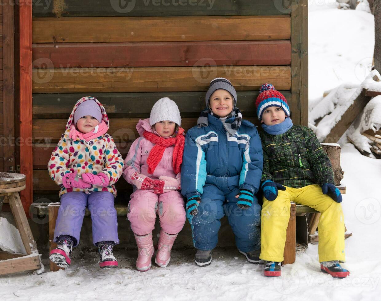 little children group sitting  together  in front of wooden cabin photo